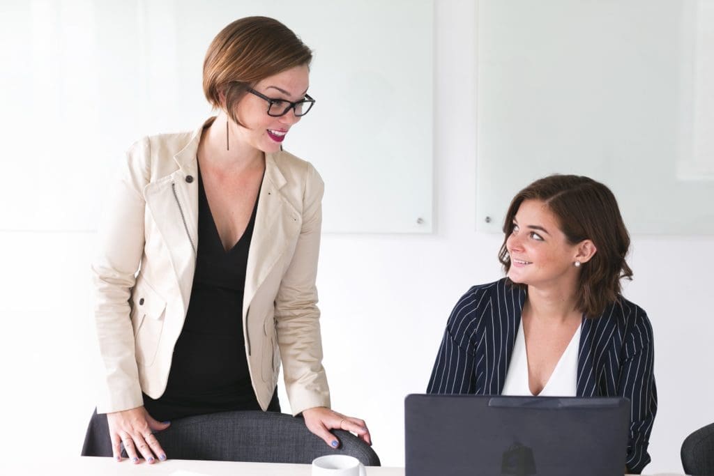 Two business women discussing work at a table in an office setting.