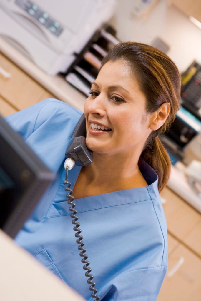 A smiling dental receptionist assisting a patient at the front desk.