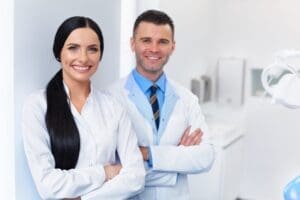 Two dentists in white coats examining a patient in a dental office, with dental equipment visible in the background.