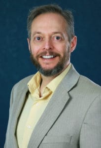 Professional portrait of a man in business attire, smiling confidently.