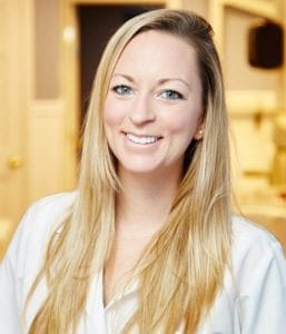 A smiling female dental professional interacting with a patient in a modern office reception area.