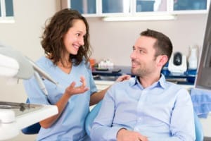 Woman talking with male patient in dental chair.