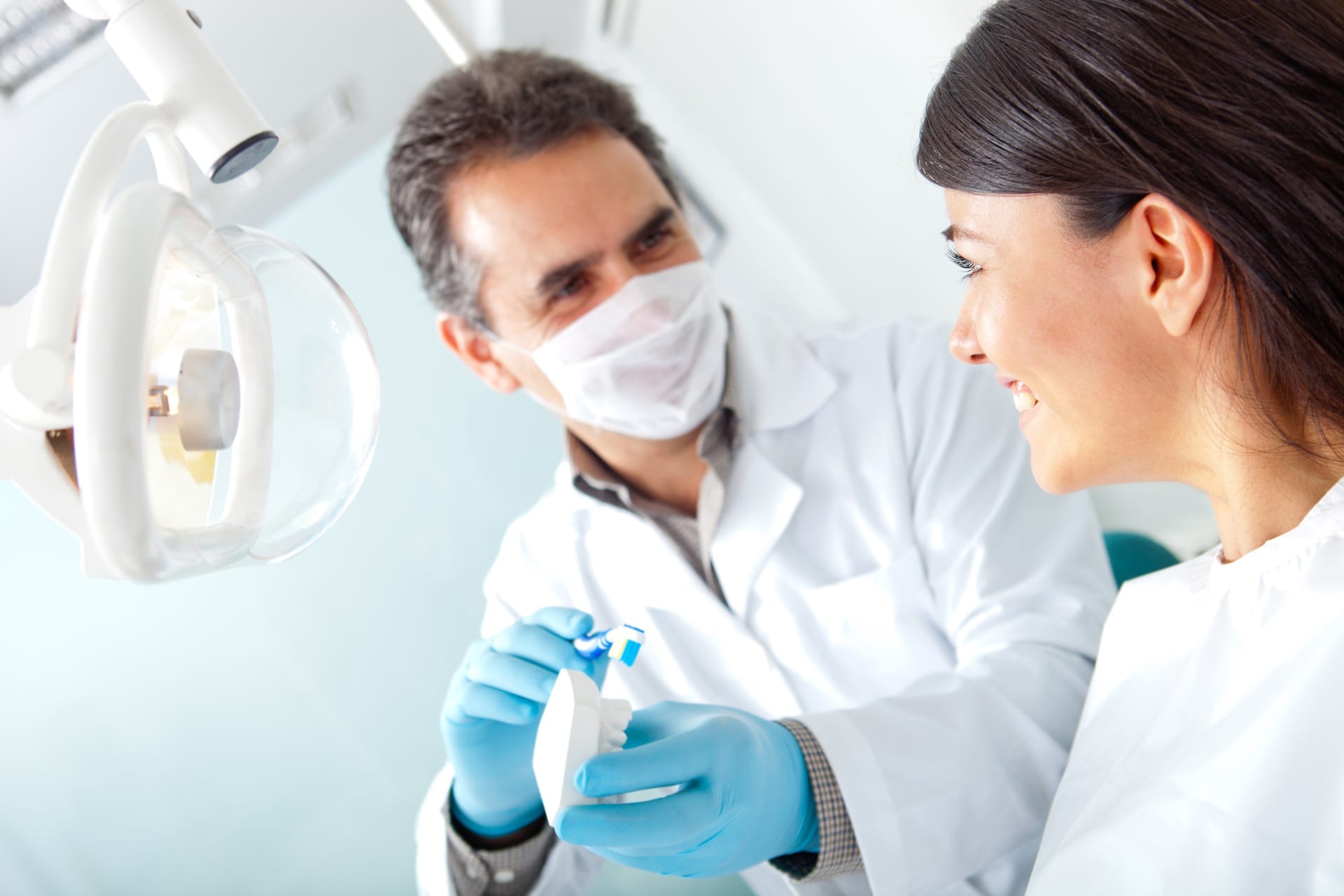 Dentist performing procedure, holding a fake set of teeth showing patient something.