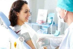 A young female patient receiving dental examination from a dentist in a clinic setting.