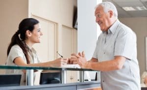 A friendly dental receptionist assisting a patient at the front desk.