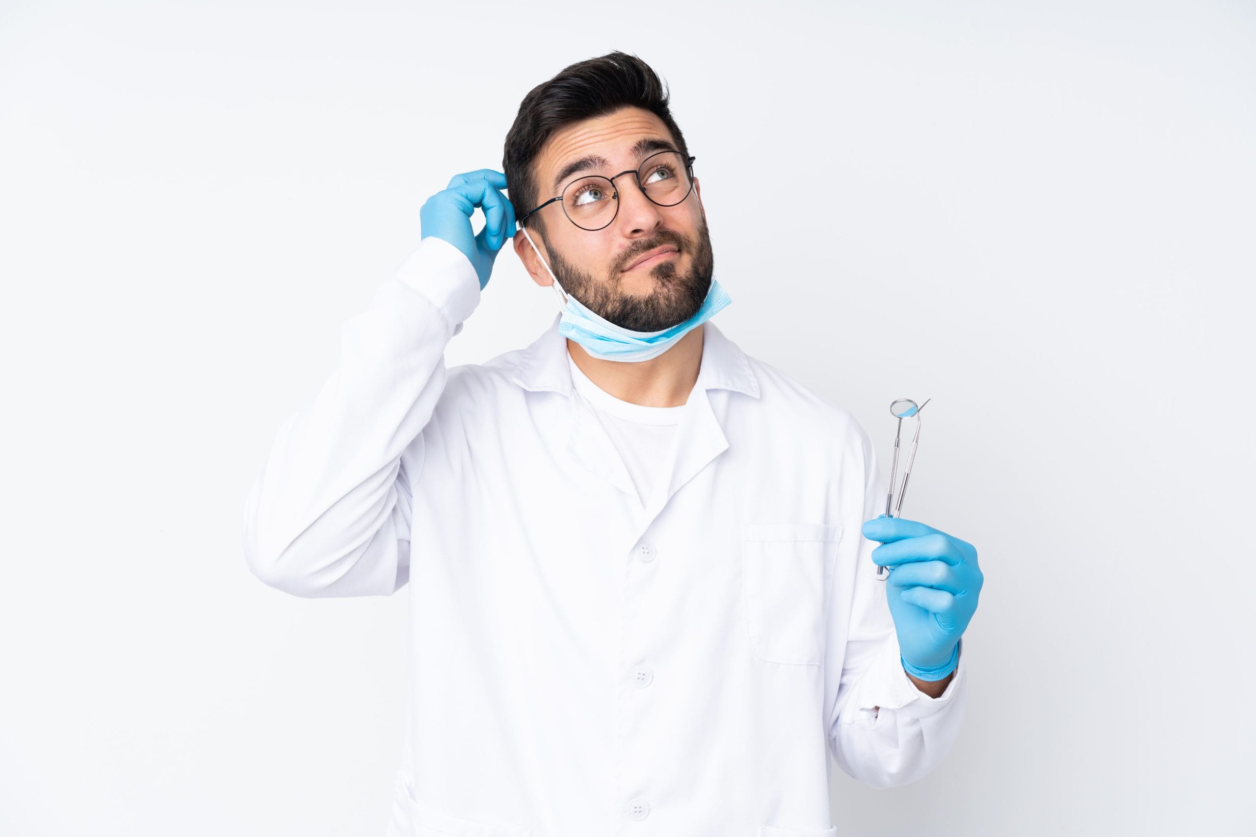 Male dentist with beard, standing and looking uncertain, holding dental equipment.
