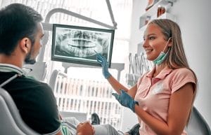 A dentist and patient seated in an examination room, reviewing a digital treatment plan on a screen.