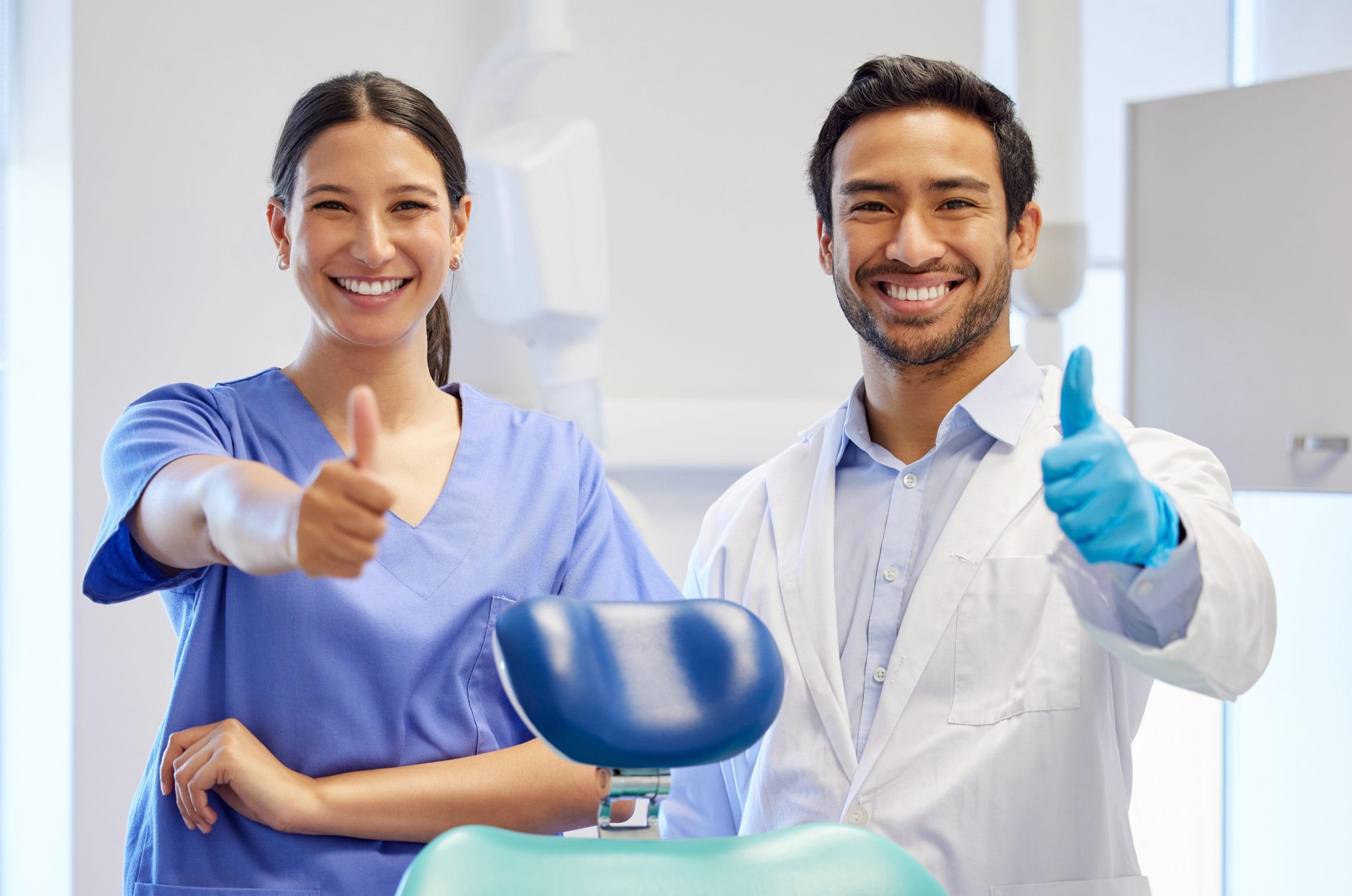 Dentist and nurse facing camera, smiling and thumbs up.