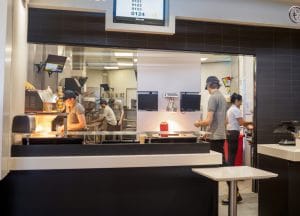 Interior of a fast food restaurant with a single employee at the cash register and a team in the kitchen.