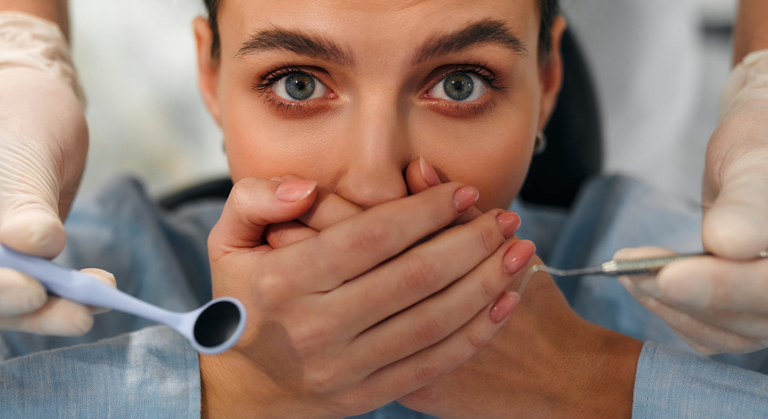 A woman covering her mouth while holding a dental pick and a water pick.