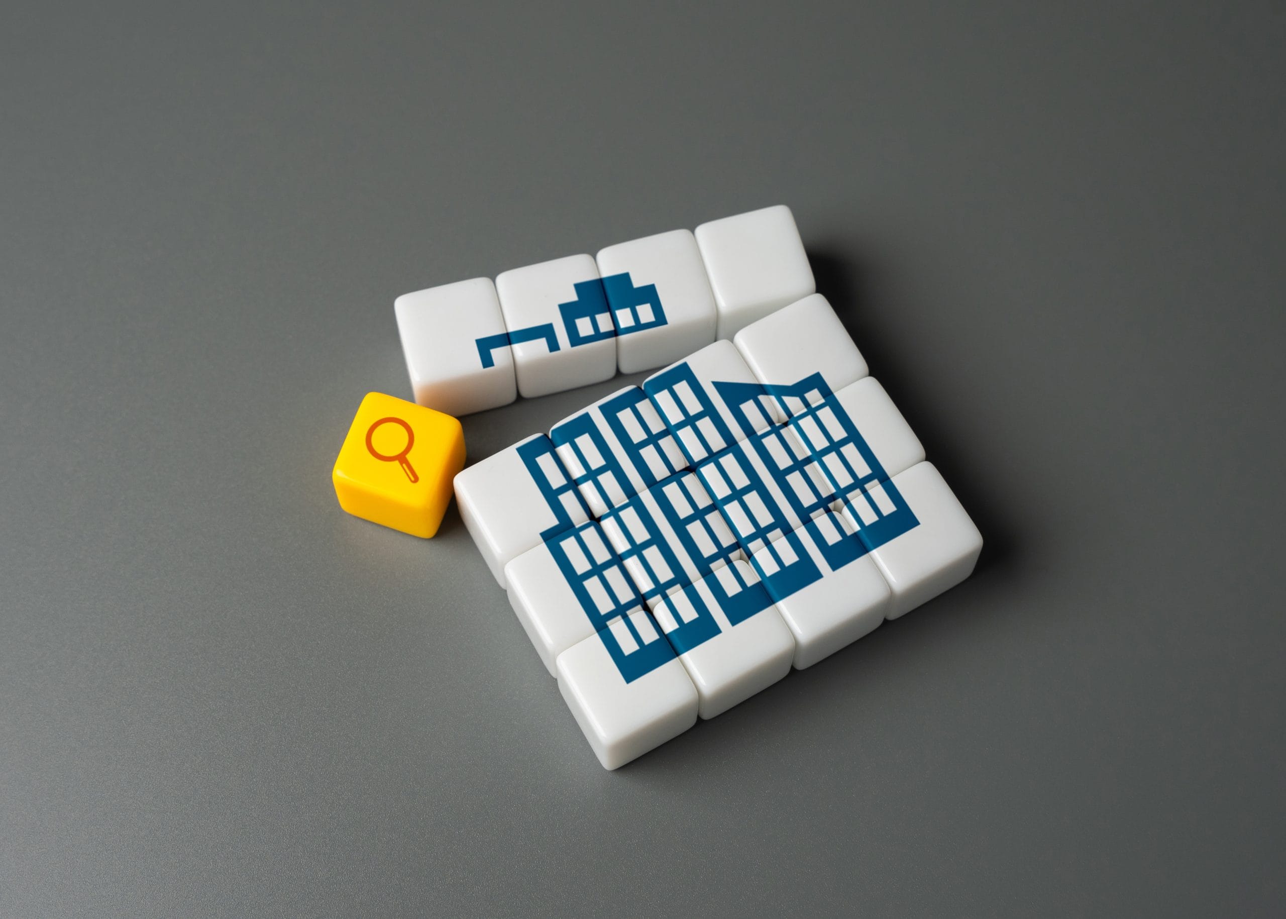 Blocks forming a blue building structure with a magnifying glass icon over one block, symbolizing inspection.