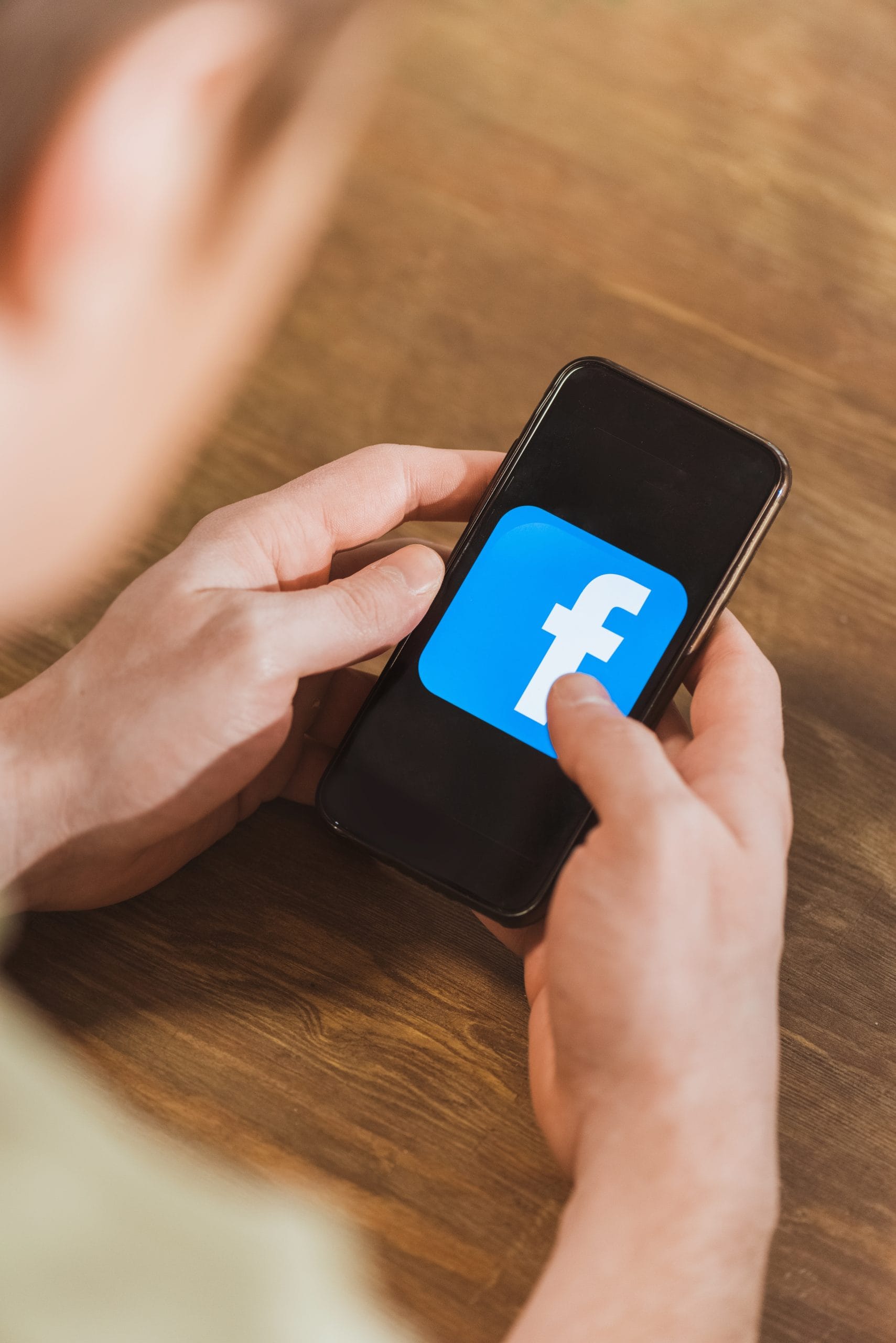 Hands holding a cell phone with a large Facebook logo on the screen