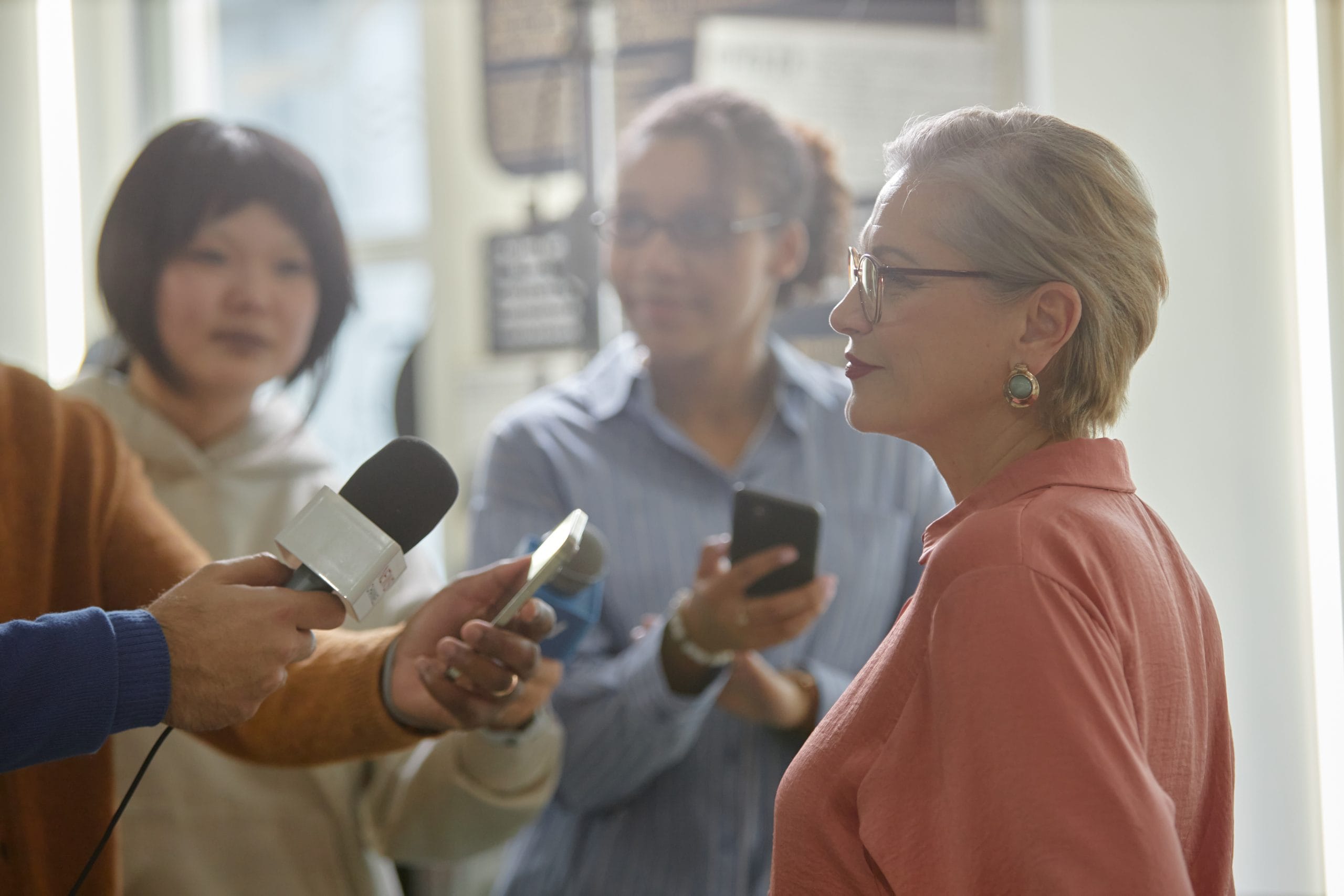A middle-aged Caucasian woman giving an interview to reporters holding microphones.