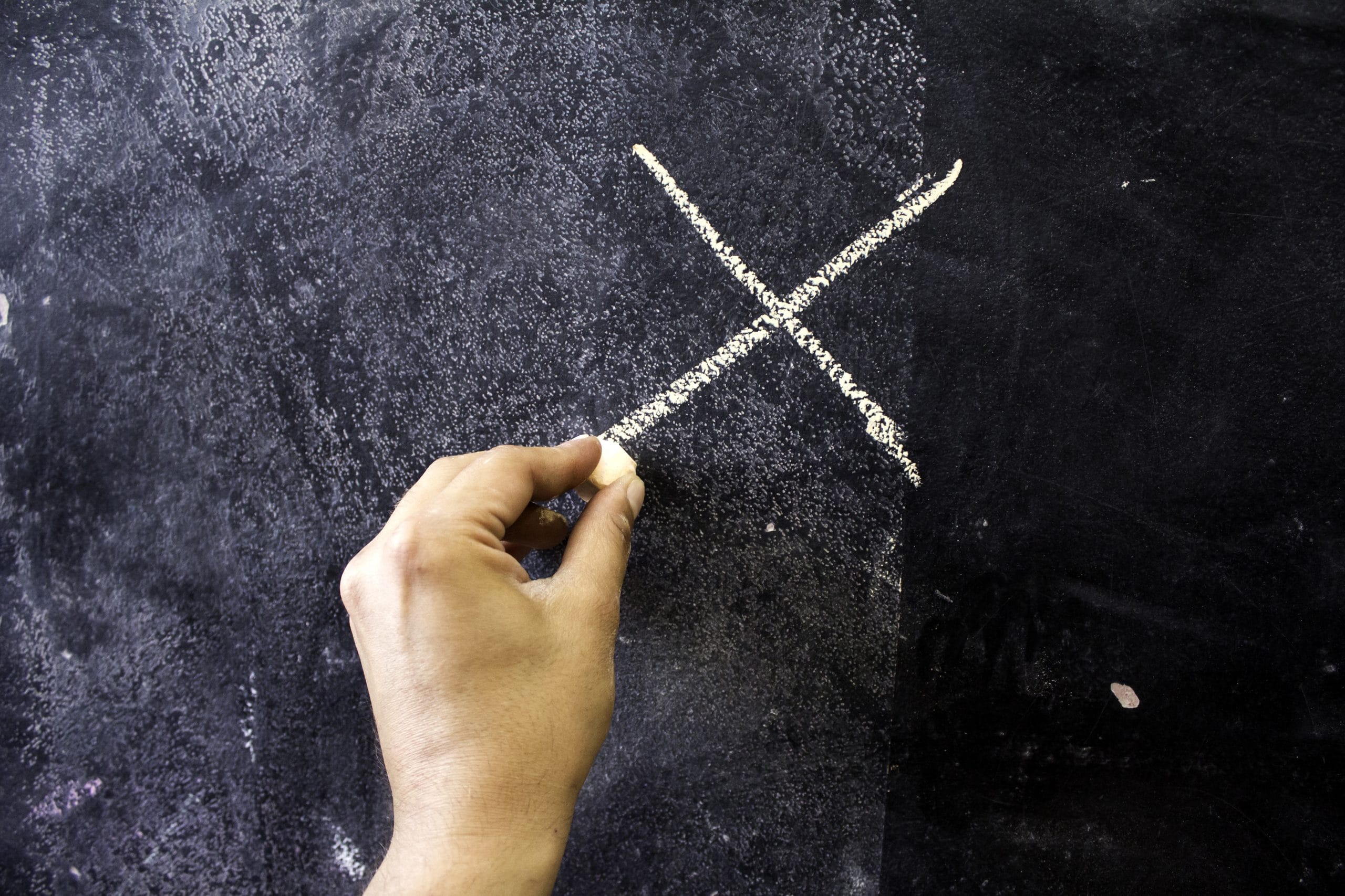 A person's hand writing an X on a chalk board.