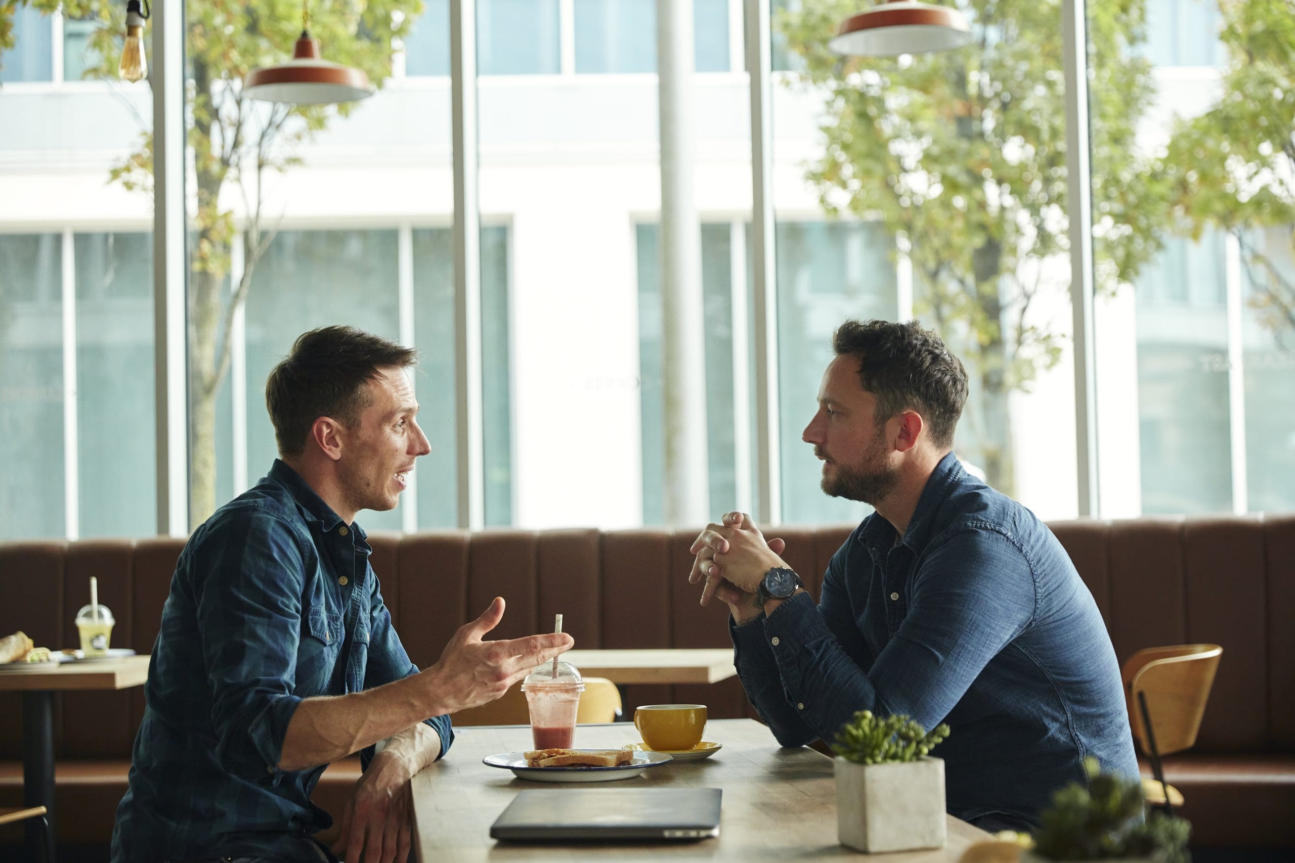 Two men seated in a cafe, talking during a meeting.