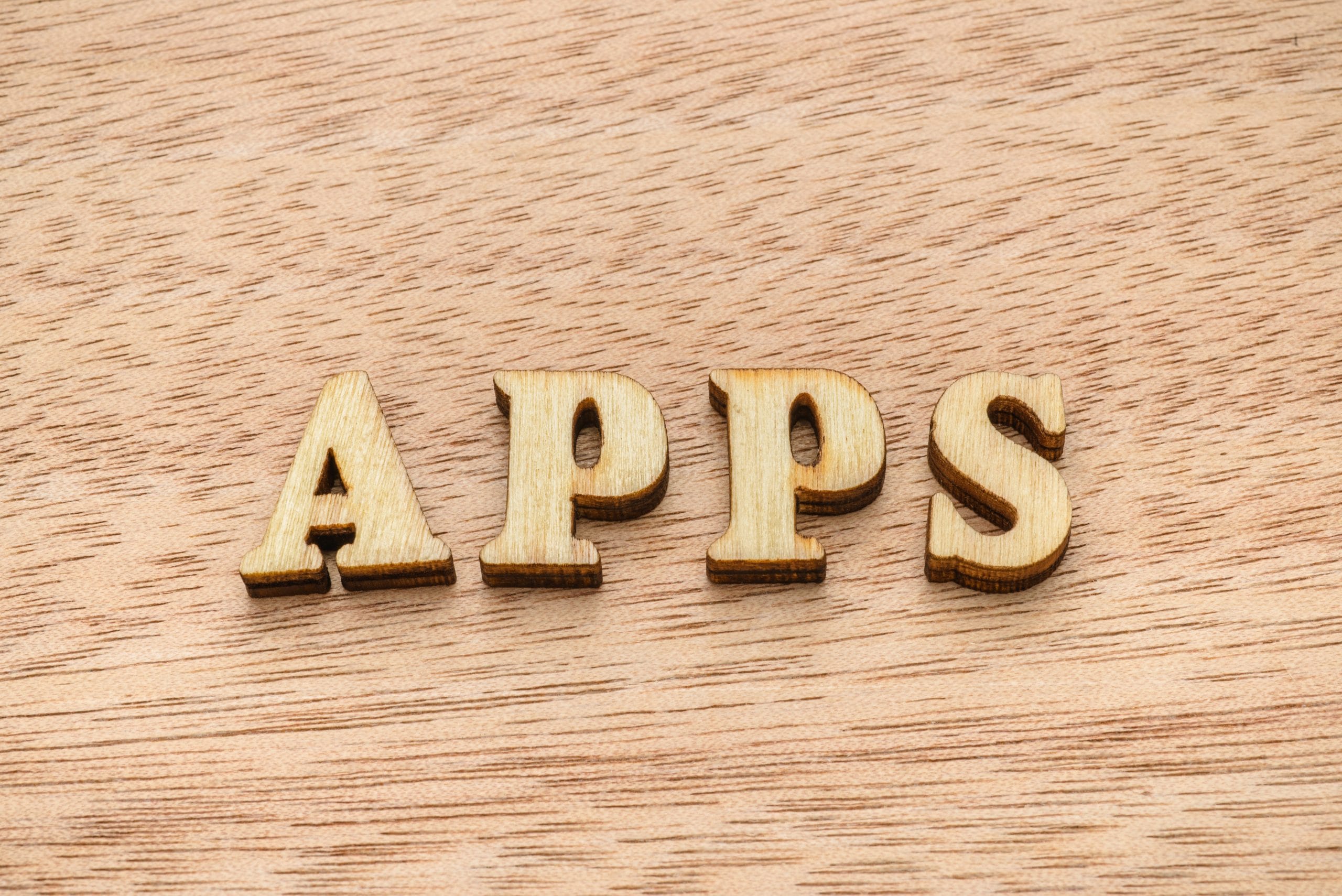 Set of wooden letters spelling the word APPS on wooden background.